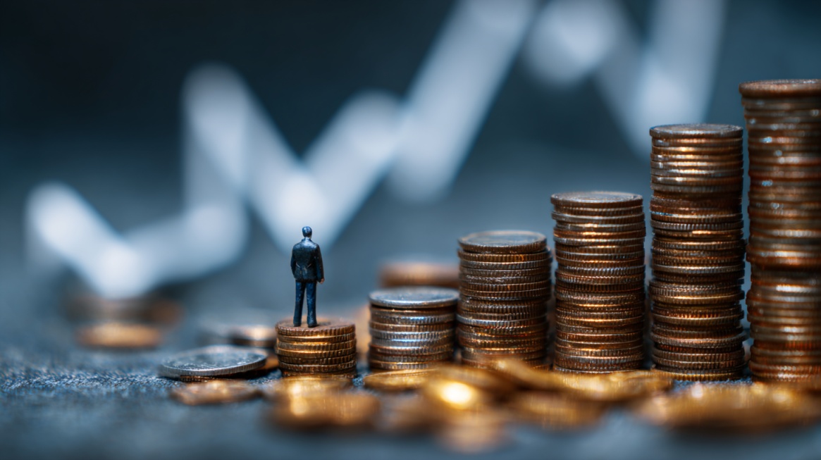 A miniature figure standing on stacks of coins arranged in increasing height, with a blurred upward graph in the background