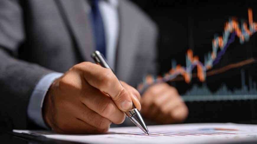 A person in a suit analyzing financial charts while writing notes with a pen