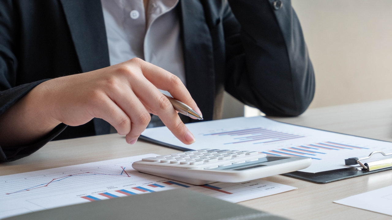 Person uses a calculator over financial charts to work out product cost per unit