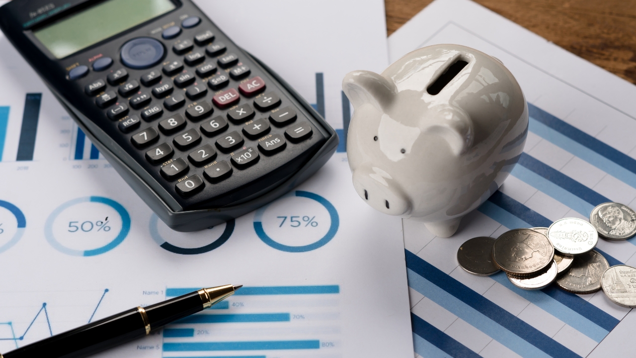 Calculator, piggy bank, and coins on financial charts show budgeting and pricing calculations